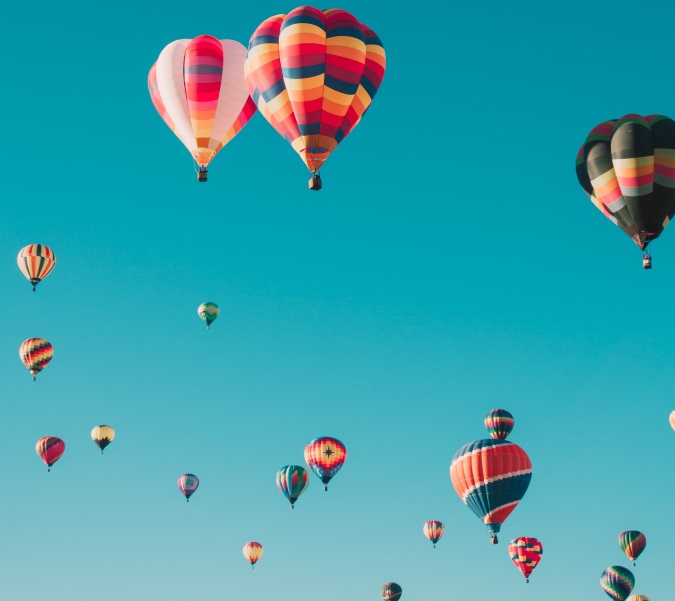 A cluster of colourful hot air balloons ascending into a clear bl